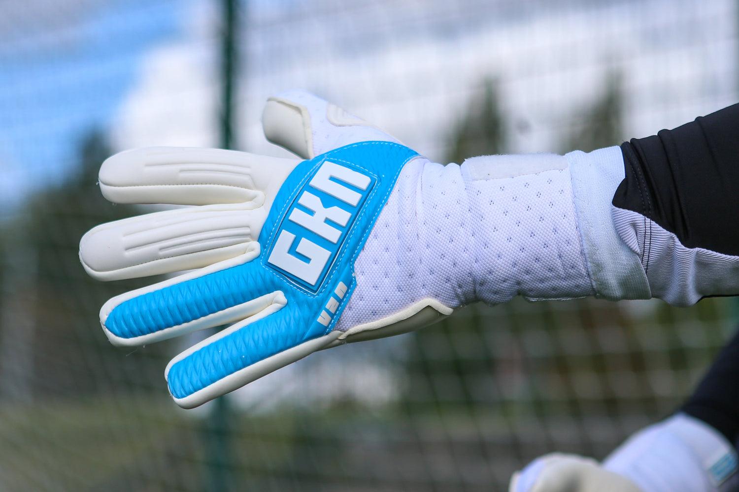 Close-up of a GKN football glove with white and black design, featuring red GKN logo on the backhand. Black textured material lines the fingers, and the glove includes padded grip sections for control and durability.