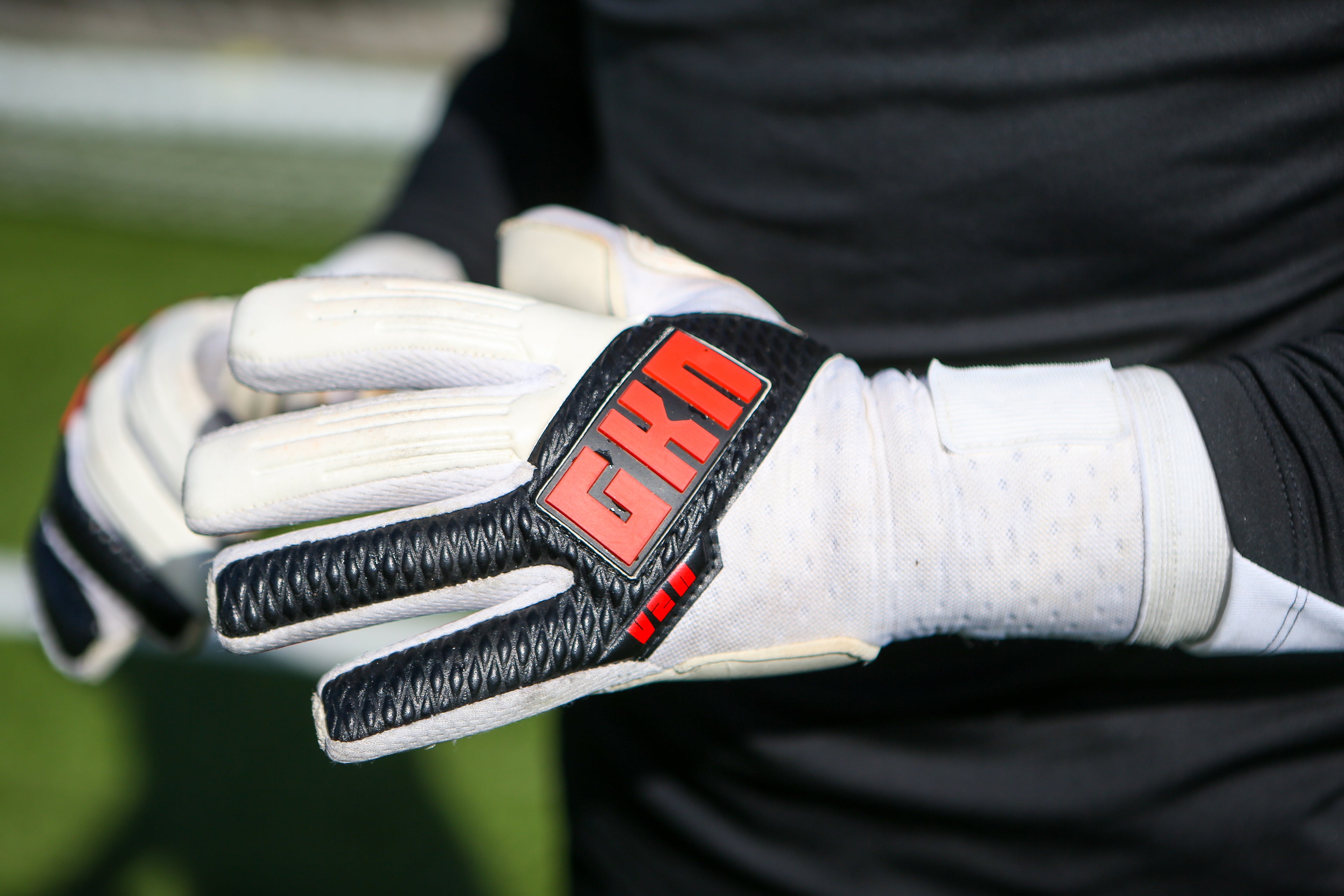 Close-up of a GKN football glove with white and black design, featuring red GKN logo on the backhand. Black textured material lines the fingers, and the glove includes padded grip sections for control and durability.